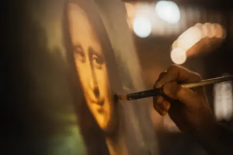 Dłoń artysty dopracowuje słynny obraz Leonarda da Vinci, Mona Lisę, dodając ostatnie pociągnięcia pędzlem.