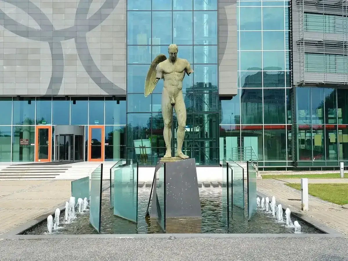 Anielskie dzieła Igora Mitoraja przed nowoczesnym budynkiem z lustrzaną fasadą.