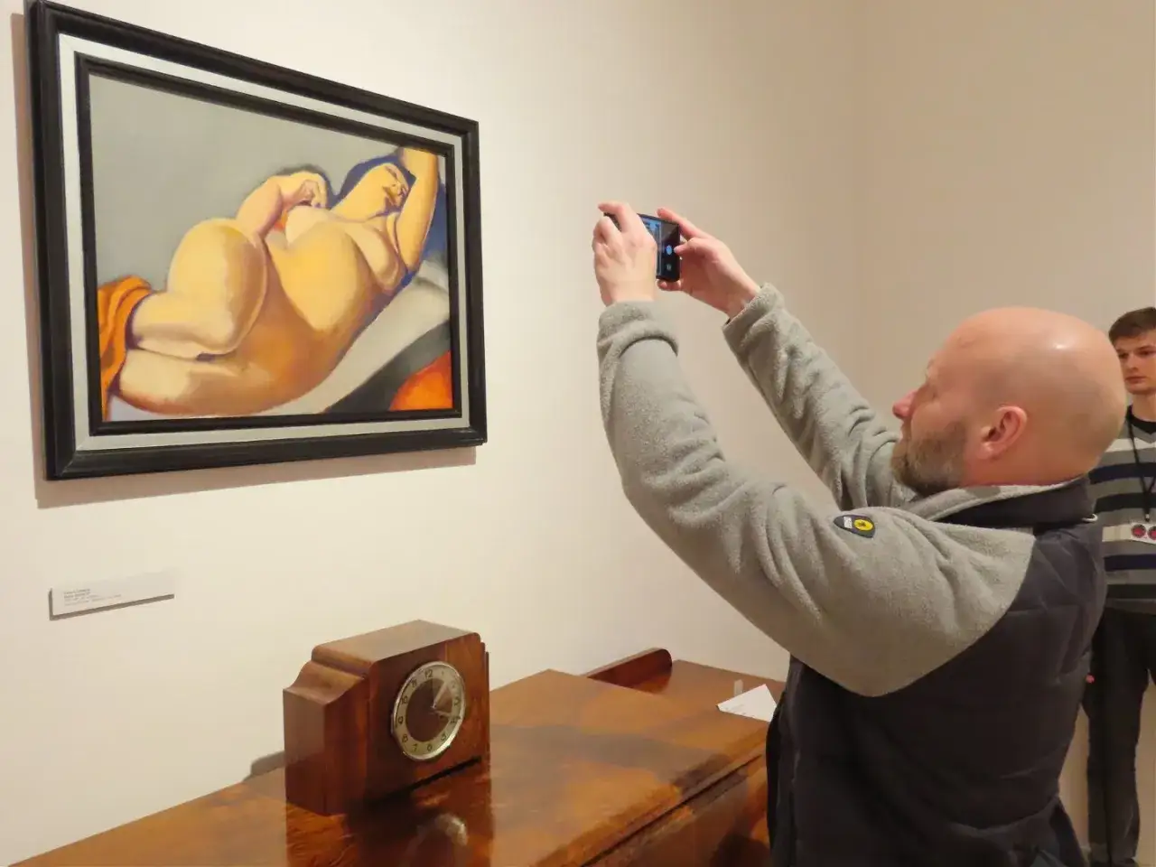 Mężczyzna fotografuje telefonem obraz tamary łempickiej w galerii.