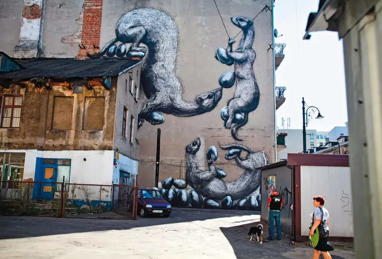 Niesamowite street art przedstawiający łasice bawiące się jajkami na ścianie kamienicy.